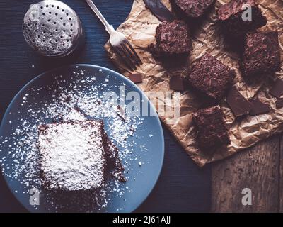 l'immagine mostra una vista dall'alto di brownie fatte in casa decorate con polvere di zucchero su tavola rustica di legno; alcuni più brownie su carta da forno; shaker aggiuntivo o Foto Stock