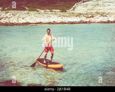 uomo che mostra come alzarsi su paddle board vicino alla spiaggia con bel mare sullo sfondo Foto Stock