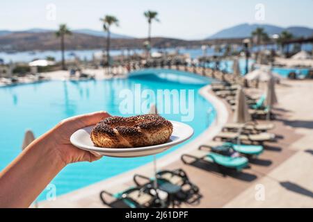 Bagel turco su un piattino in mano sullo sfondo del mare blu e palme. Carattere nazionale. Foto Stock