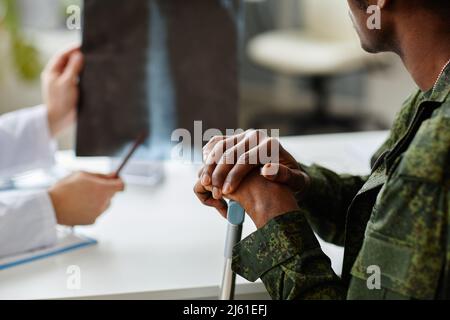 Uomo militare inriconoscibile ferito utilizzando bastone a piedi seduto di fronte al medico che ha parlato di chirurgia Foto Stock