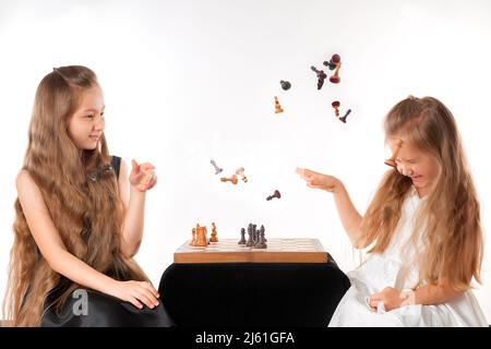 Le sorelle delle bambine giocano a scacchi su sfondo bianco. Concetto di sport e hobby. Sviluppo cognitivo. Gioco intellettuale. Bambini intelligenti. Foto Stock