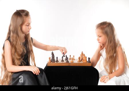 Le sorelle delle bambine giocano a scacchi su sfondo bianco. Concetto di sport e hobby. Sviluppo cognitivo. Gioco intellettuale. Bambini intelligenti. Foto Stock