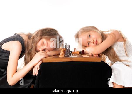 Le sorelle delle bambine giocano a scacchi su sfondo bianco. Concetto di sport e hobby. Sviluppo cognitivo. Gioco intellettuale. Bambini intelligenti. Foto Stock