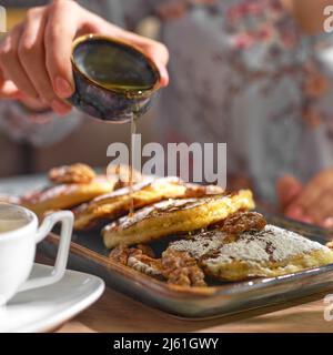 Donna che versa miele dolce su gustosi pancake sul piatto, primo piano. Foto Stock