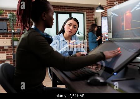 Sviluppo di giochi creativi artisti di agenzia che parla di livello design e 3D risorse mentre si siede in ufficio spazio di lavoro. Lavoratori del settore dell'intrattenimento digitale interattivo che lavorano con CGI. Foto Stock