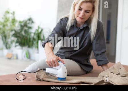 la donna utilizza una macchina per la rimozione di pellet e bobine da vestiti e tessuto su pantaloni neri. Un moderno dispositivo elettronico per aggiornare le cose vecchie. Foto Stock