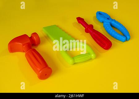 Giochi di riparazione colorati su sfondo giallo, gioco del bambino isolato su sfondo giallo, idea di gioco, pinza cacciavite colorato sega martello, vista dall'alto Foto Stock