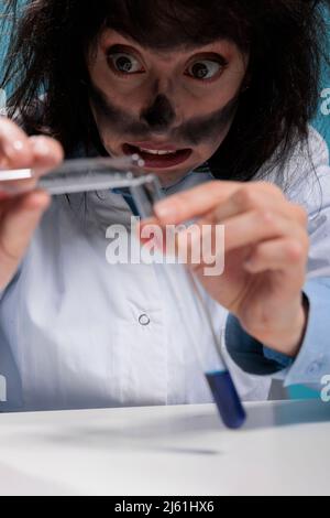 Primo piano di un chimico malgolo che mescola sostanze chimiche per creare una nuova formula utilizzando composti sconosciuti. Divertente scienziato pazzo sperimentare con fluidi tossici è risultato da un'esplosione di laboratorio Foto Stock