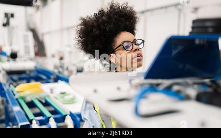 Ingegnere che indossa occhiali esaminando la macchina robotica a braccio in fabbrica Foto Stock