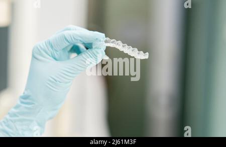 Dentista che indossa guanti protettivi che reggono l'allineatore dentale in clinica Foto Stock