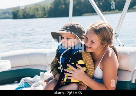 Bambino ragazzo carino seduto sul grembo delle donne su barca di fiume Foto Stock