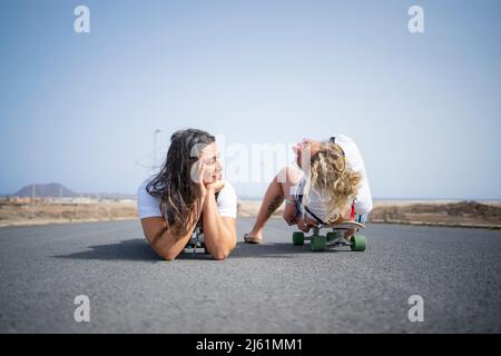 Amici con skateboard sdraiati su strada Foto Stock