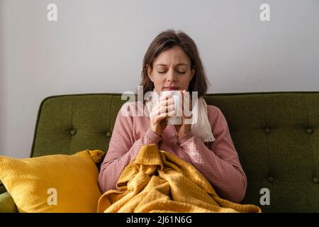 Donna malata con tazza di tè seduta sul divano a casa Foto Stock