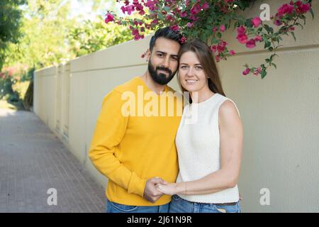 Coppia sorridente che tiene le mani in piedi davanti al muro Foto Stock