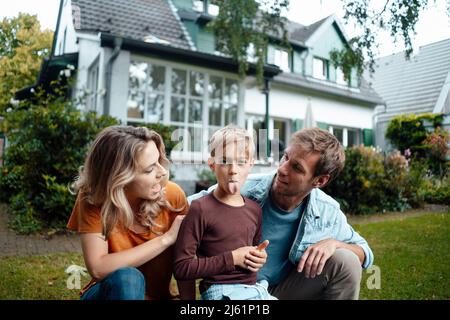 Madre e padre che guardano il figlio che sporge la lingua sul cortile Foto Stock