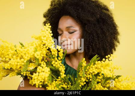 Giovane donna che odora mimosa fiori su sfondo giallo Foto Stock