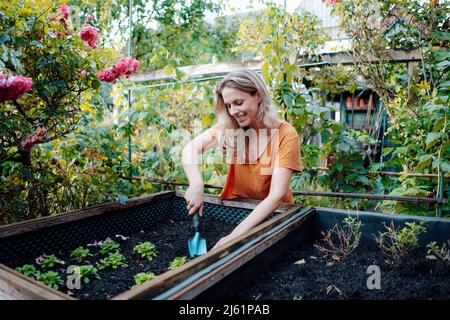 Donna bionda sorridente con pala giardinaggio in cortile Foto Stock