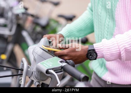 Mano di uomo che noleggia bicicletta tramite telefono cellulare presso la stazione di parcheggio Foto Stock