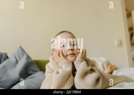 Ragazzo che indossa un pullover oversize con la testa in mano sul letto a casa Foto Stock