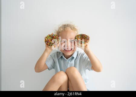 Ragazza felice che tiene le ciambelle seduti davanti al muro Foto Stock