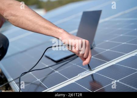 Ingegnere che collega il caricabatterie del cavo di alimentazione del laptop ai pannelli solari Foto Stock