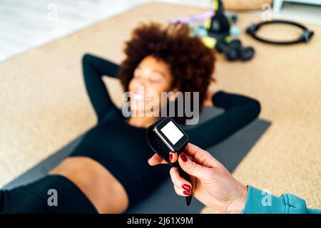 Donna che tiene smart watch da un amico che fa esercizio a casa Foto Stock