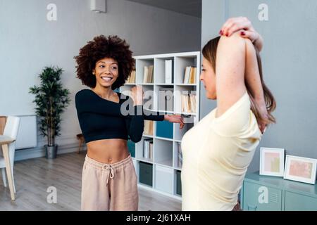 Giovane donna felice con un amico che allunga le braccia in salotto a casa Foto Stock