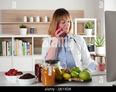 distratto nutrizionista femminile chiacchierando con smartphone in studio Foto Stock