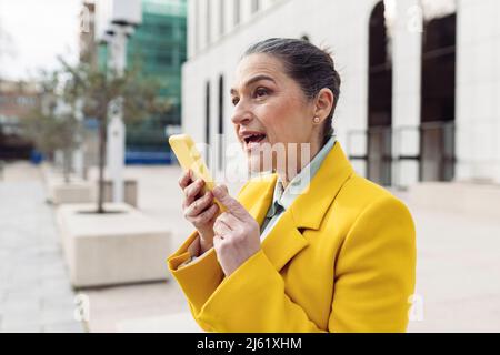 Donna d'affari che invia messaggi vocali tramite telefono cellulare presso il parcheggio dell'ufficio Foto Stock