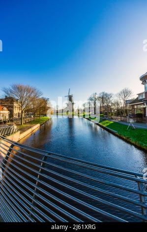 Paesi Bassi, Sud Olanda, Leiden, cielo trasparente sul canale della città con mulino a vento sullo sfondo Foto Stock