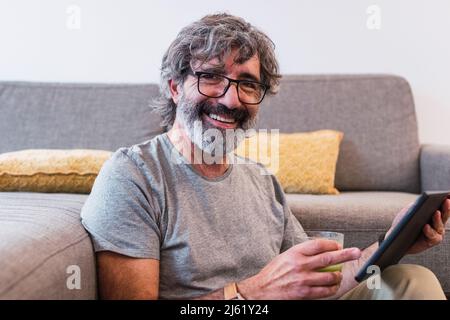 Uomo con tablet PC seduto a terra sul divano di casa Foto Stock
