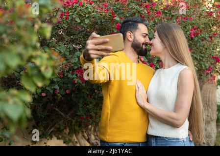 Coppia eterosessuale sfregamento nosi e prendere selfie su smartphone in giardino Foto Stock