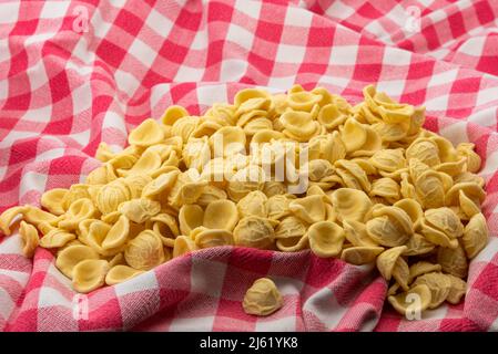 Orecchiette su tovaglia a scacchi rossi, pasta italiana pugliese a base di farina di grano duro e acqua, tipica della cucina pugliese Foto Stock