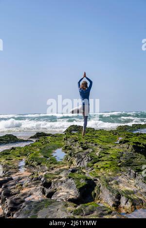 Donna in piedi su roccia praticare albero posa fare yoga in spiaggia Foto Stock