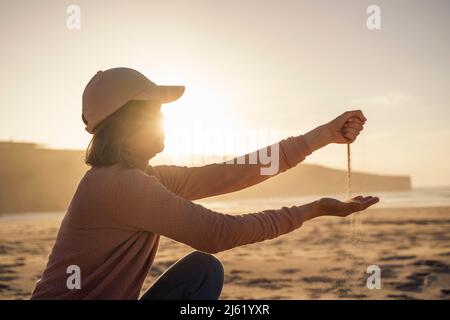 Sabbia che cade dal pugno chiuso della donna al tramonto Foto Stock