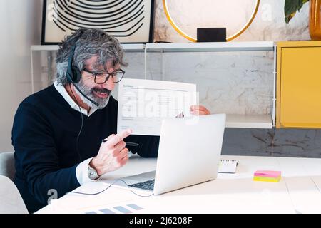 Un freelance sorridente con documenti che fanno videochiamate attraverso il laptop a casa Foto Stock