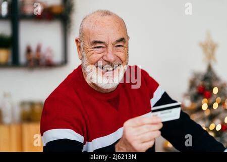 Uomo anziano felice che detiene la carta di credito a casa Foto Stock