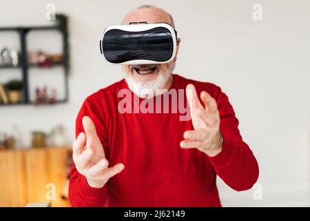 Uomo anziano felice che indossa simulatore di realtà virtuale gesturing a casa Foto Stock
