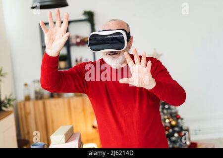 Uomo anziano che indossa simulatore di realtà virtuale gesturing a casa Foto Stock