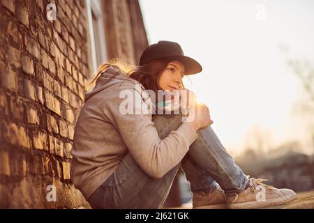 Giovane donna in attesa con cappellino da baseball seduto a terra con ginocchia abbracciate Foto Stock