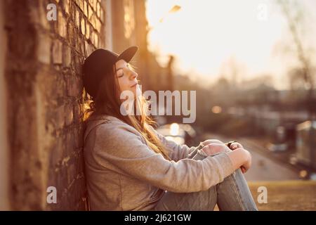 Giovane donna appoggiata su un muro di mattoni con gli occhi chiusi Foto Stock