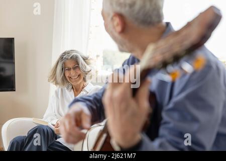 Donna felice che guarda l'uomo che suona la chitarra a casa Foto Stock