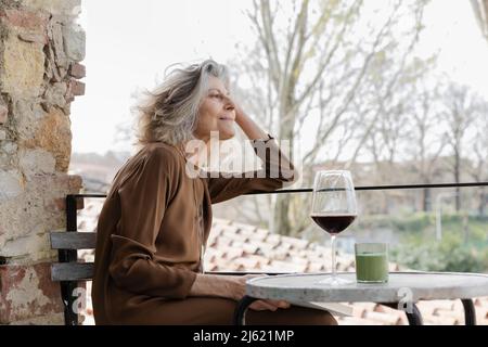Sorridente donna anziana seduta con mano in capelli al balcone Foto Stock