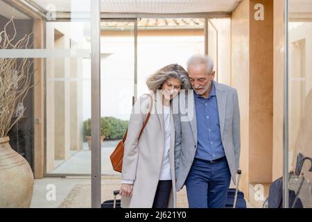 Sorridente coppia anziana che cammina con le valigie nella hall dell'hotel boutique Foto Stock