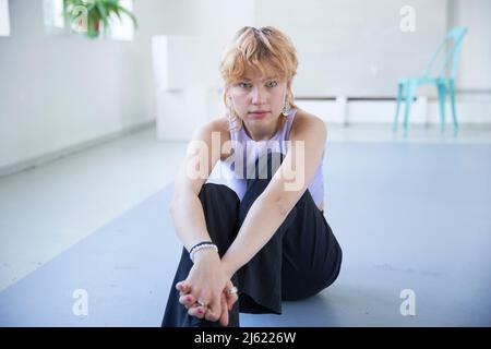 Giovane donna con le mani aggrappate seduta sul pavimento Foto Stock