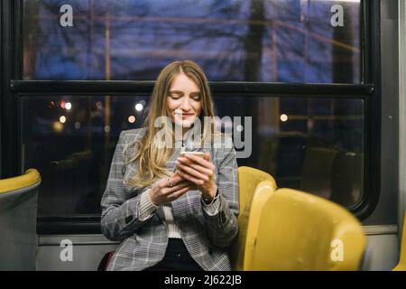 Donna sorridente con smartphone seduto in tram Foto Stock