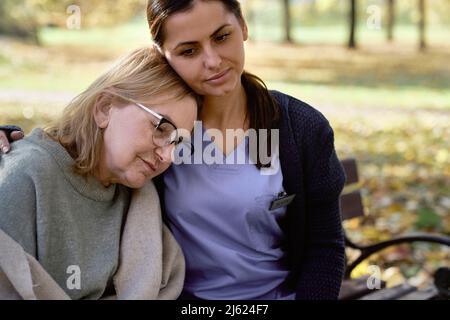 Donna anziana che indossa occhiali seduti con custode al parco Foto Stock