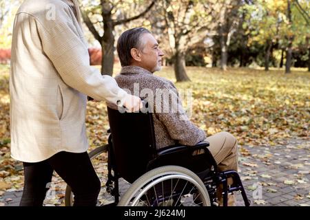 Uomo anziano disabili seduto in sedia a rotelle spinto da una donna al parco Foto Stock