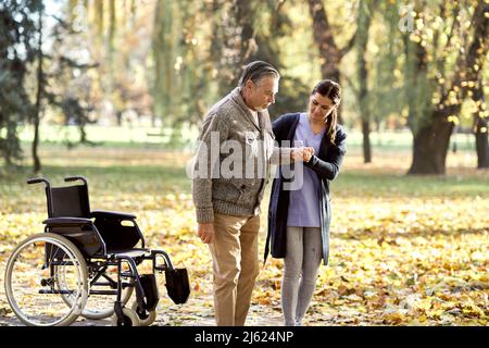 Operatore sanitario che aiuta gli anziani disabili a camminare nel parco Foto Stock