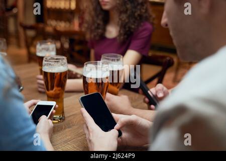 Amici che hanno birra e usare smartphone in un pub Foto Stock